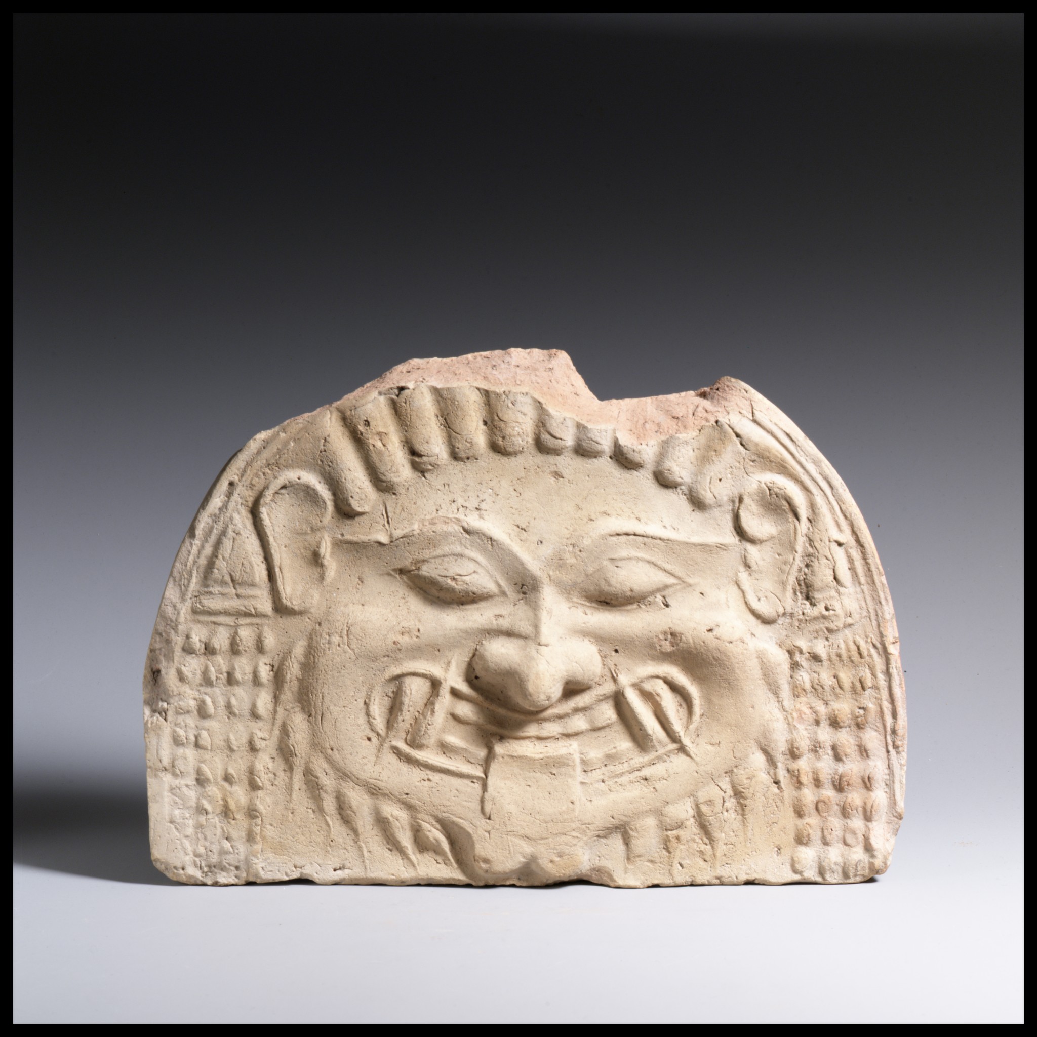 Archaic terracotta Gorgon face with large staring eyes and visible teeth