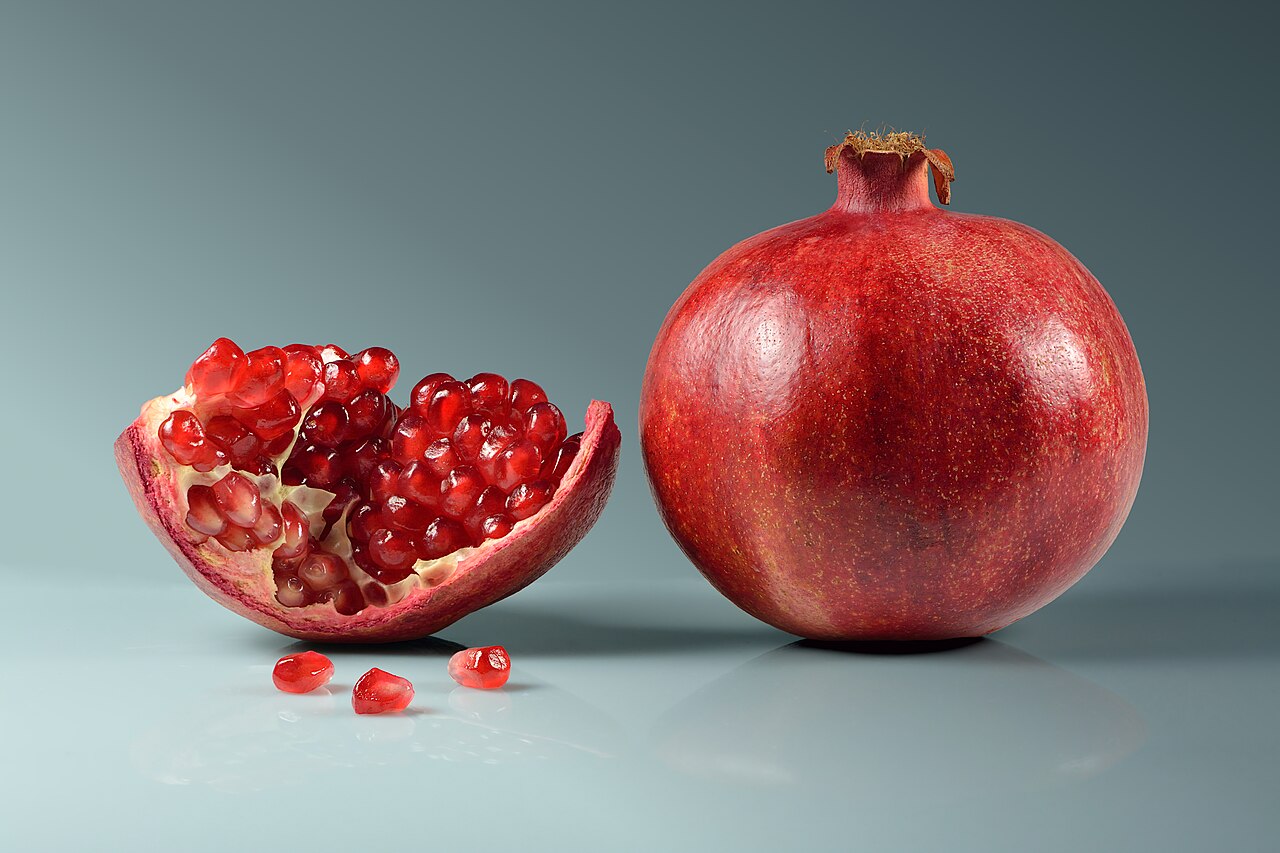 A whole red pomegranate beside an opened section filled with jewel-like arils
