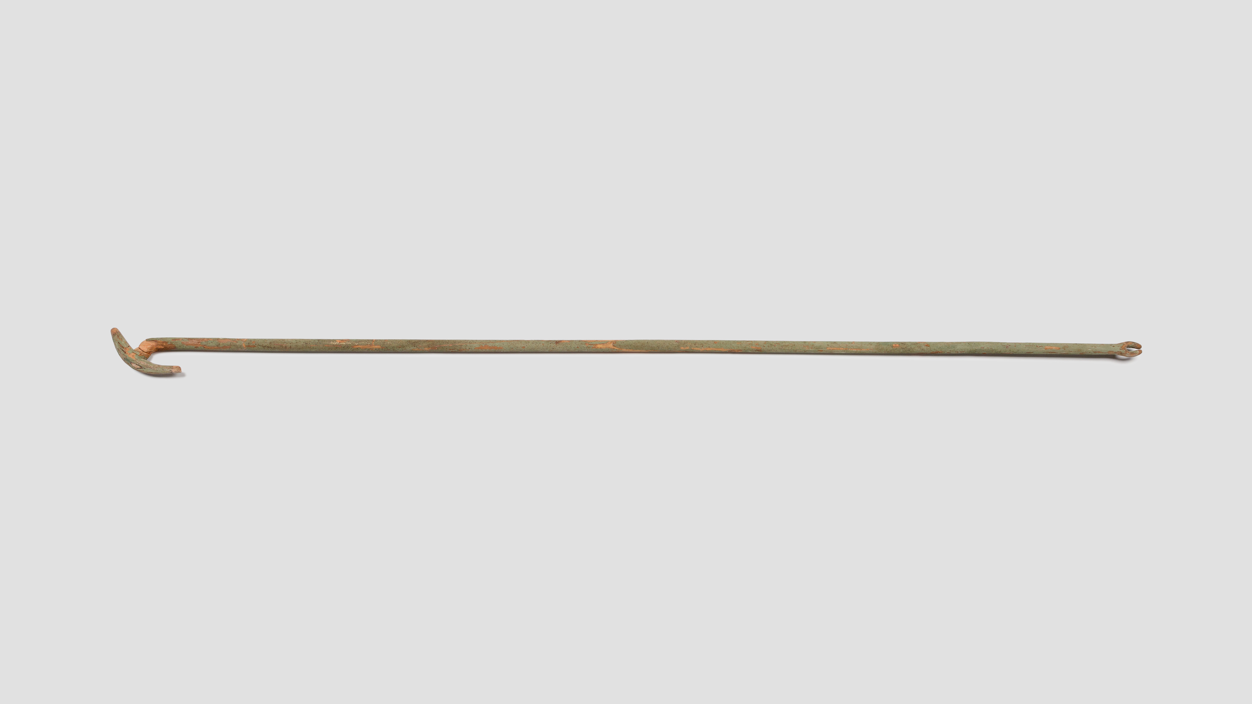 An intact ancient wooden was-sceptre photographed horizontally, showing its animal-shaped head and forked foot.