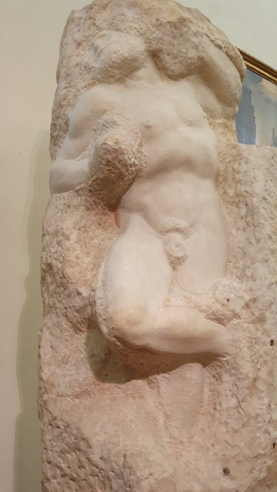 A marble sculpture still mostly inside its rough block: a powerful male figure twists and strains, his torso and one leg emerging from the uncut stone while his head and arms are still sunk in it.