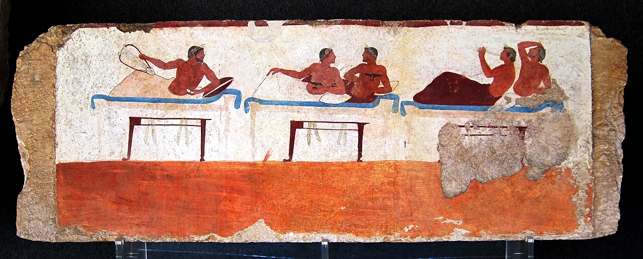 Greek fresco: 5 men recline on 3 banquet couches with wine cups and a lyre, painted in red and blue on a white ground above a red band