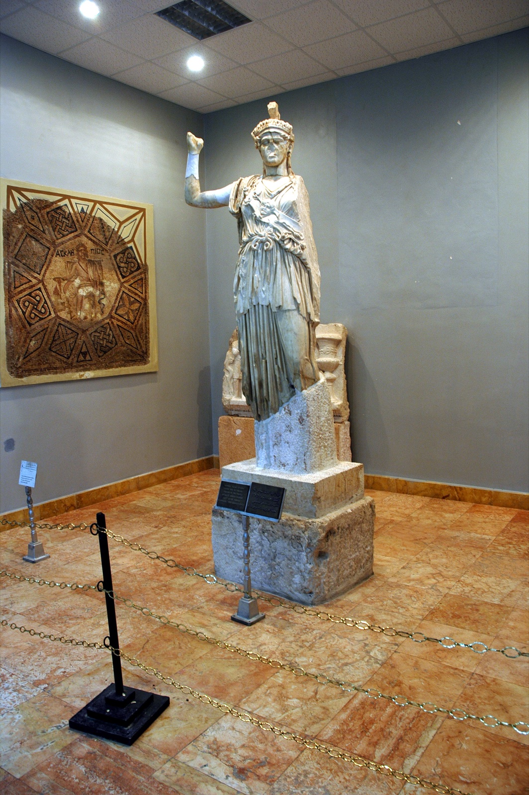 A white marble statue of Athena in a helmet and long robe with one arm raised, displayed on a pedestal in a museum gallery.