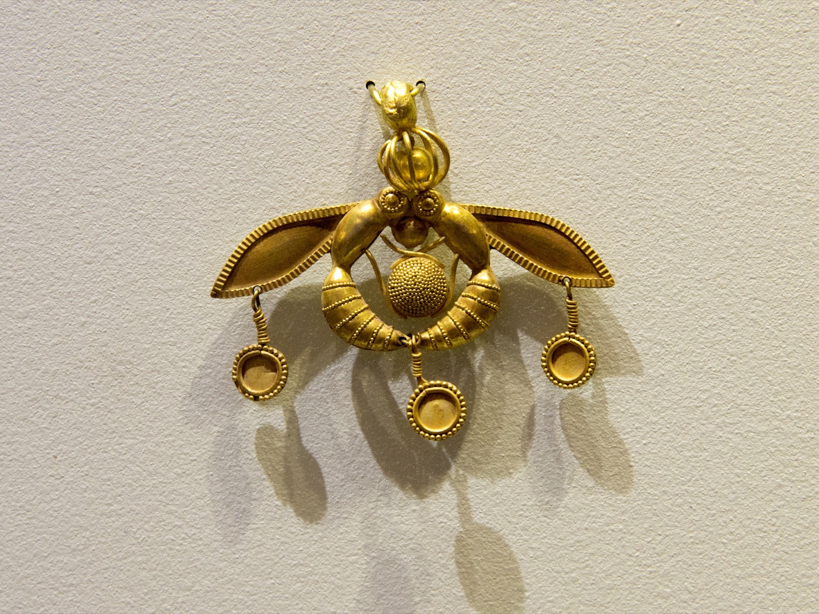 Minoan gold pendant of 2 insects facing each other, with 3 small discs hanging from their wings and joined bodies.