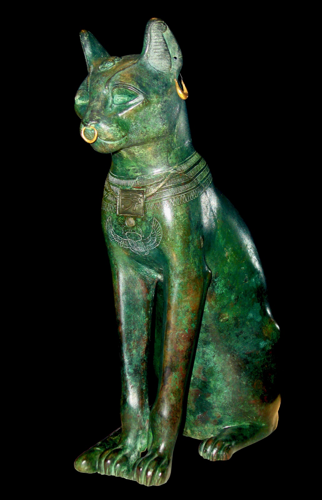 A tall seated Egyptian cat statue in dark metal, upright and alert, with gold rings in its ears and nose.