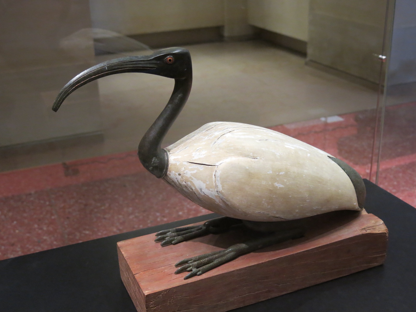 A carved statue of an ibis lying down on a base, white-painted wood combined with metal parts.