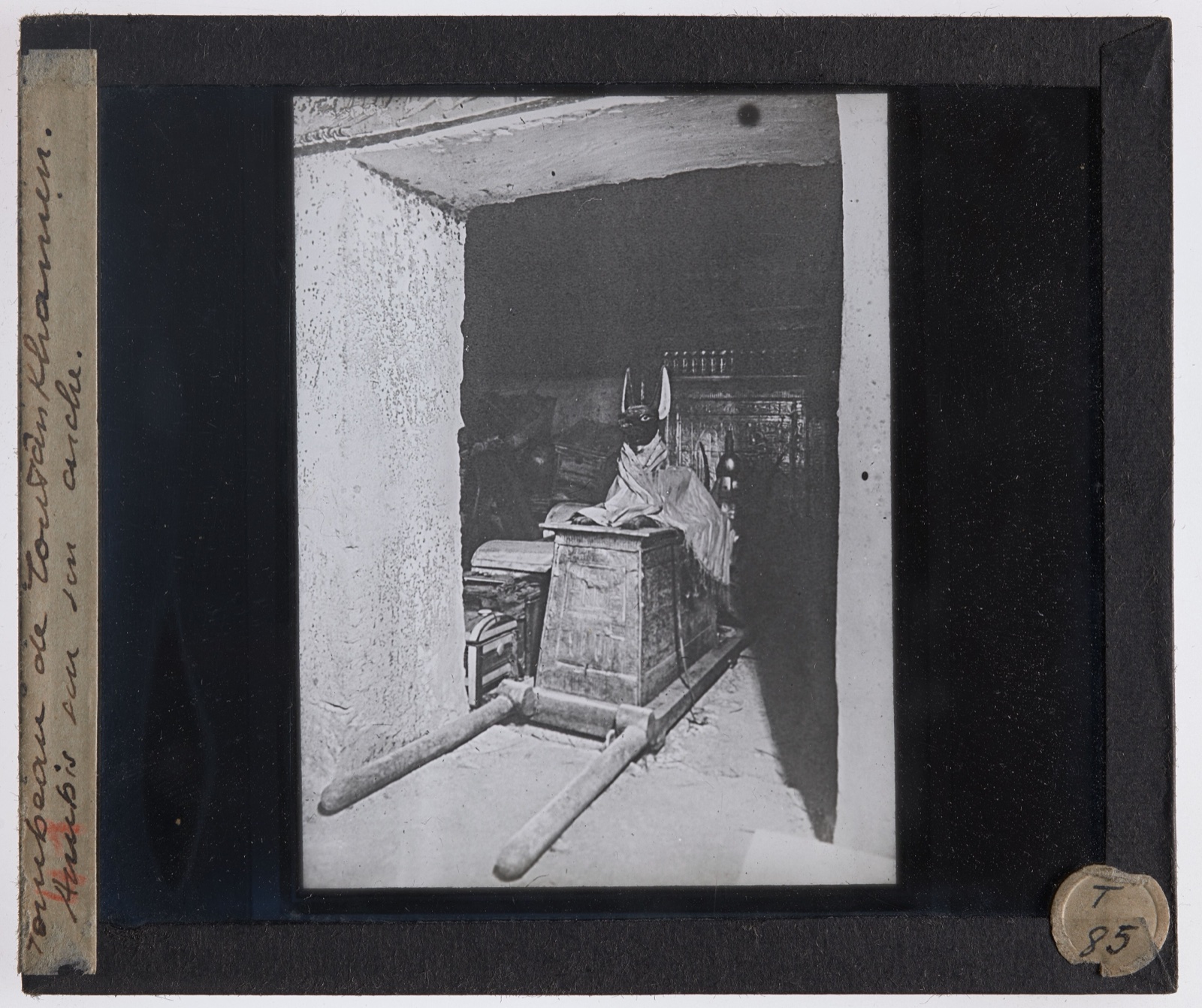 Black and white photograph of a black jackal statue lying on top of a shrine in a tomb chamber.