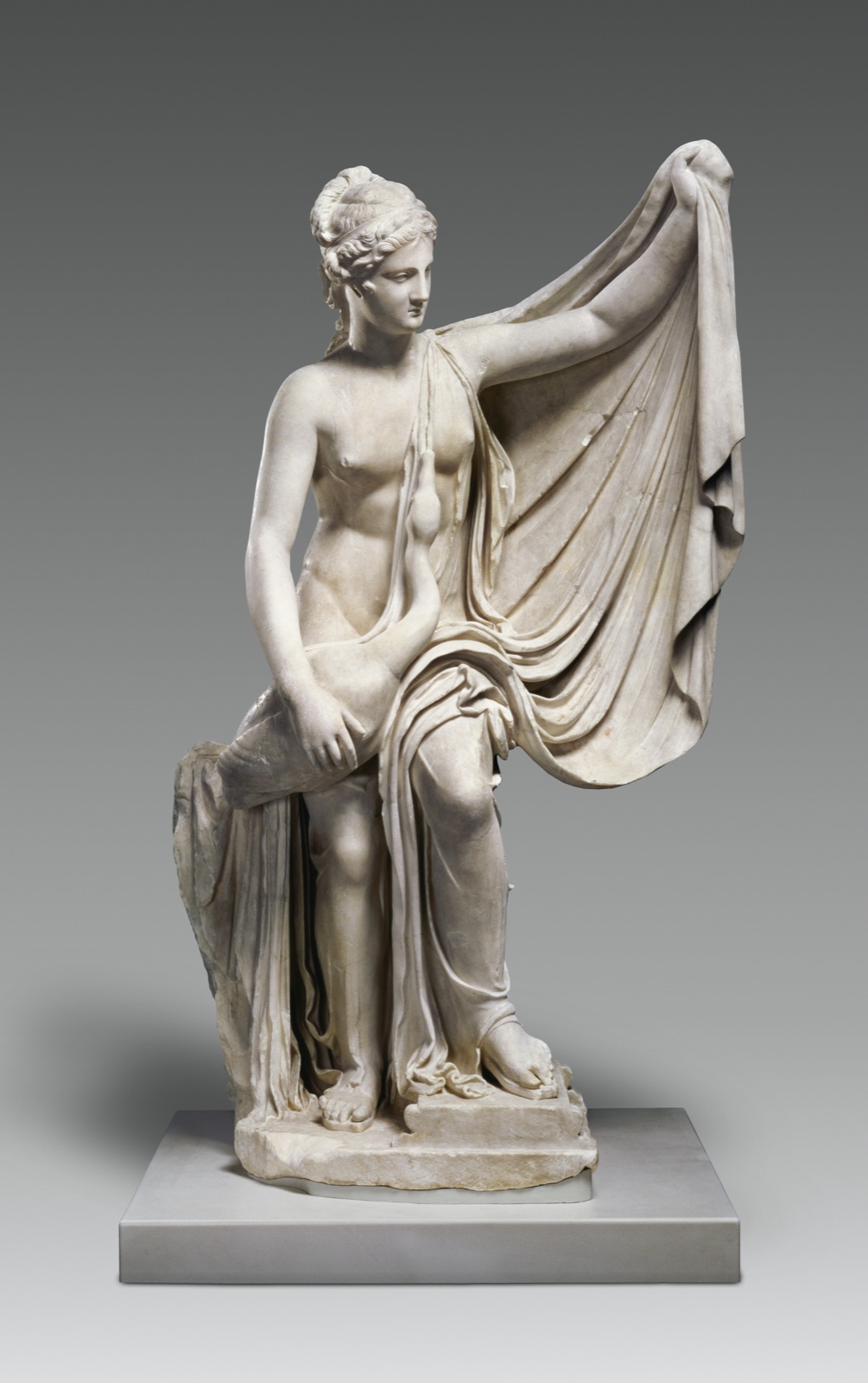 Marble statue of a standing woman holding a swan against her body beneath a raised cloak.